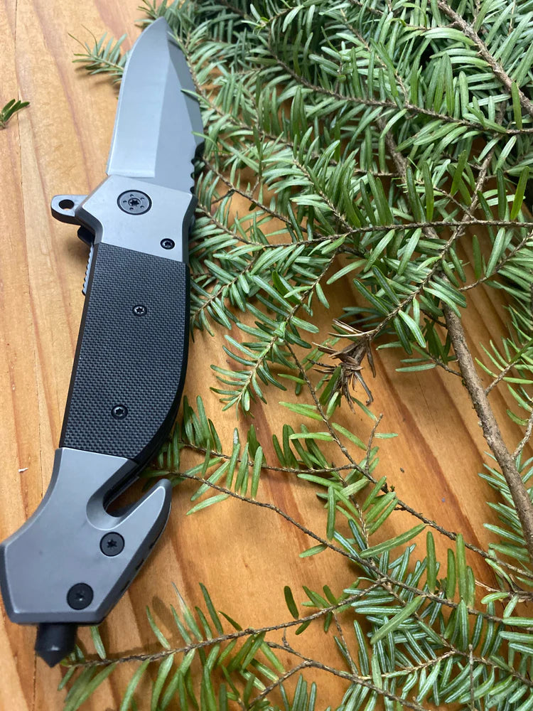  Browning Folding knife with black handle and silver blade on a wooden surface with green foliage.