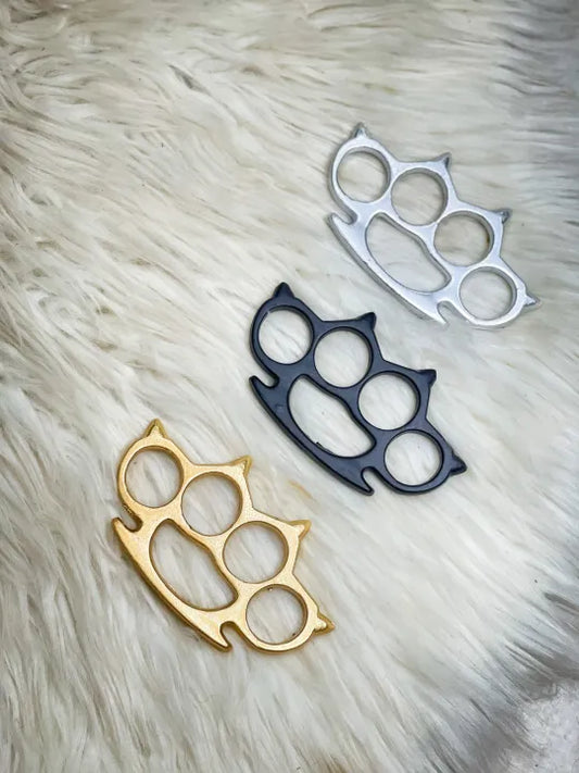 Three brass knuckles in gold, black, and silver on a fur surface.