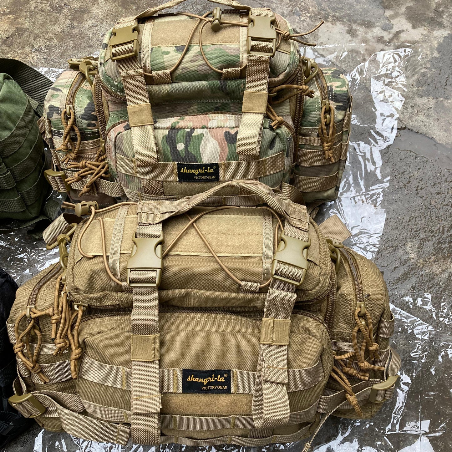 Two tactical backpacks, one camouflage and one beige, on a reflective surface.