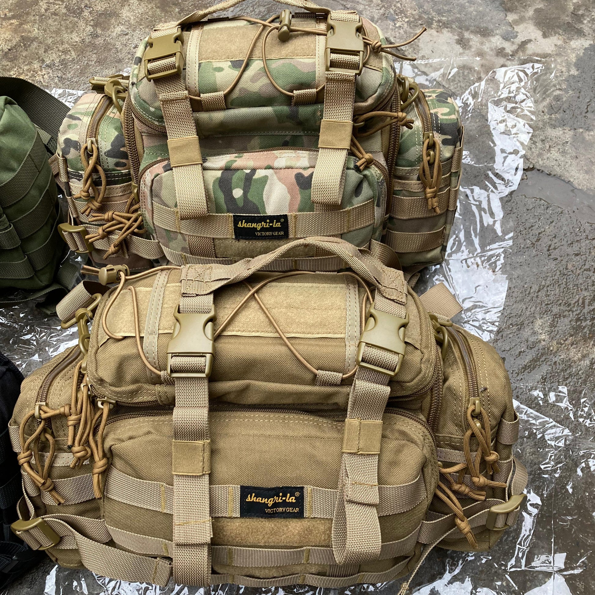 Two tactical backpacks, one camouflage and one beige, on a reflective surface.