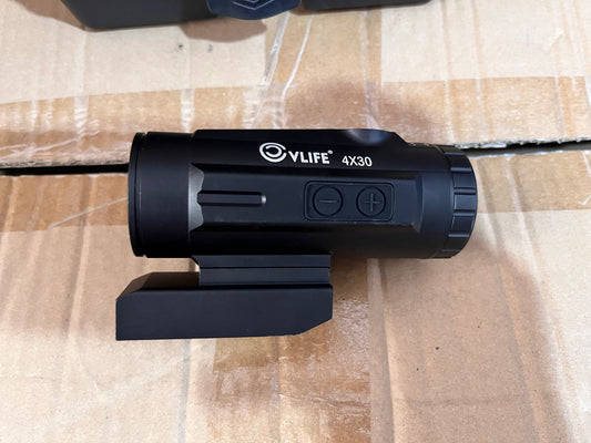 A black V-LIFE 4X30 monocular scope with a mounting bracket, resting on a brown cardboard box.